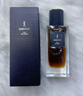 YSL Babycat Raw Bourbon Eau de Parfum bottle next to its dark navy blue box, placed on a white faux fur surface.