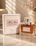 Dior Miss Dior Absolutely Blooming Eau de Parfum bottle with amber liquid and silver cap, displayed next to its white and pink packaging box on a marble surface.