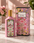 Gucci Flora Gorgeous Gardenia perfume bottle in pink with a gold cap, shown next to its matching floral-patterned box on a marble surface.