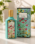 Gucci Flora Gorgeous Jasmine perfume bottle in a light turquoise color with a gold cap, shown next to its matching floral-patterned box on a marble surface.