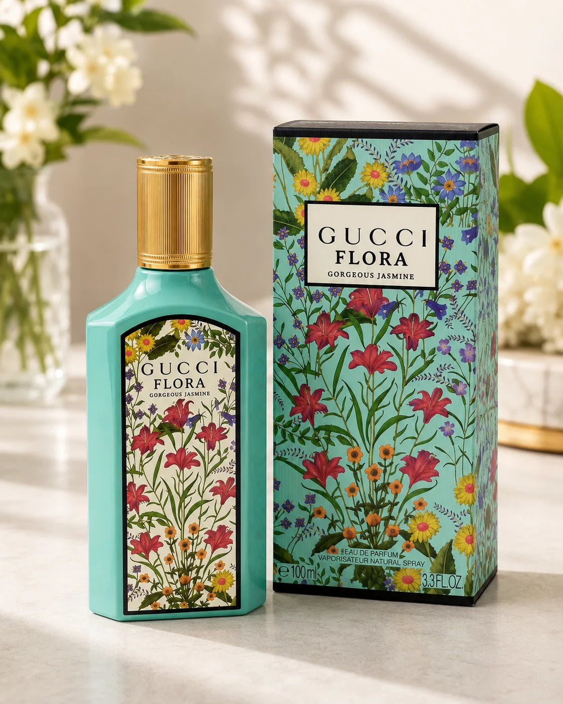 Gucci Flora Gorgeous Jasmine perfume bottle in a light turquoise color with a gold cap, shown next to its matching floral-patterned box on a marble surface.