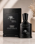 Creed Absolu Aventus fragrance bottle and its black textured packaging box, displayed on a light marble surface with a soft beige background and dried floral decor.