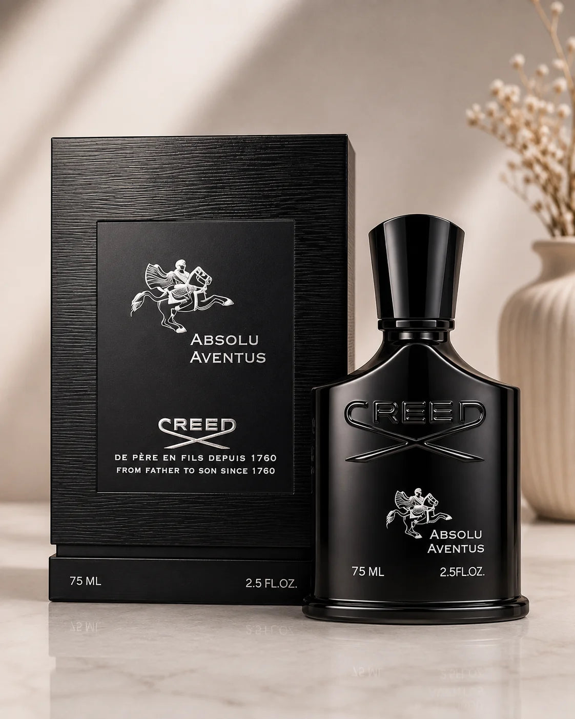 Creed Absolu Aventus fragrance bottle and its black textured packaging box, displayed on a light marble surface with a soft beige background and dried floral decor.