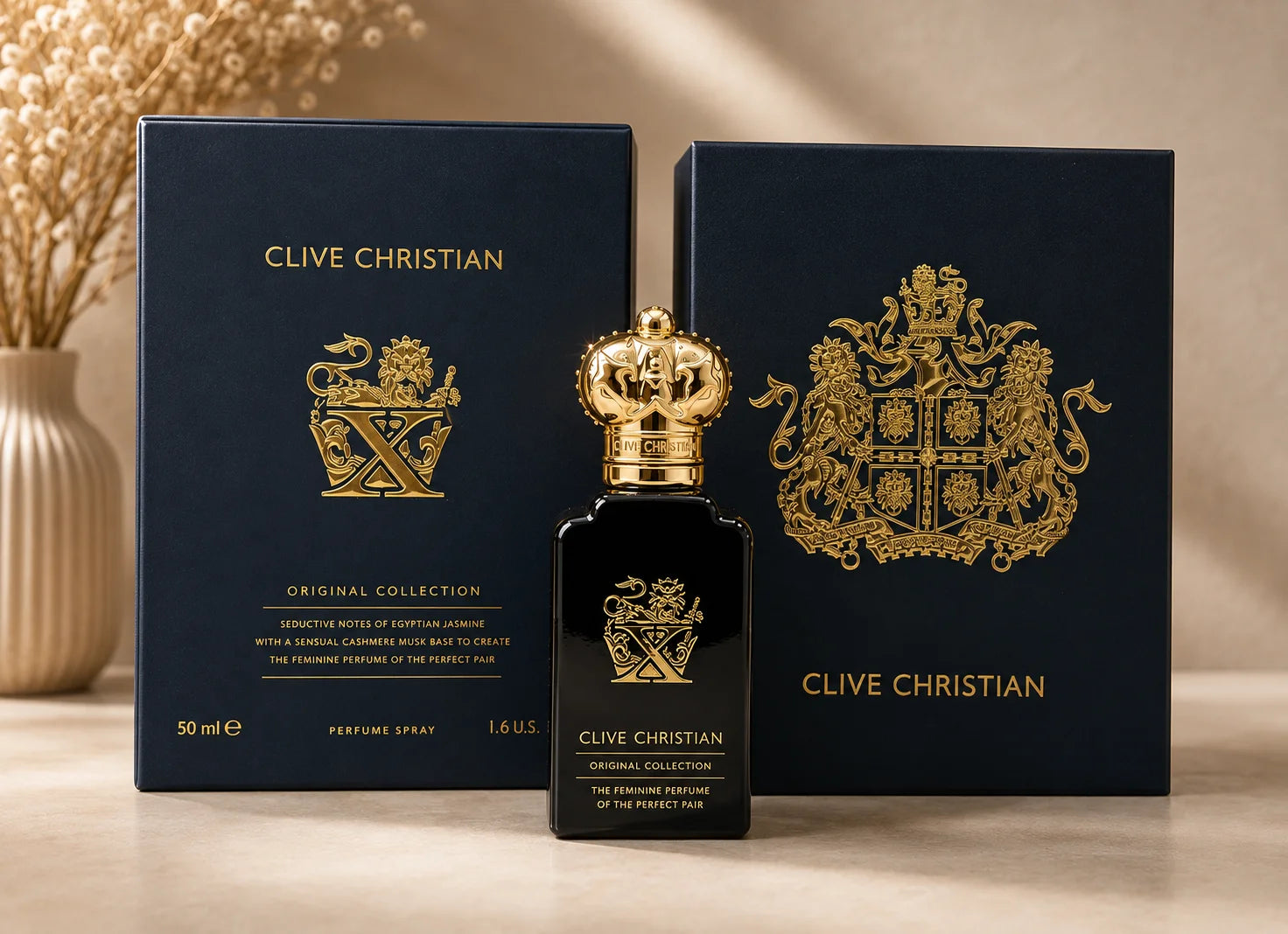 A bottle of Clive Christian Original Collection perfume stands centered between two dark navy blue boxes with gold crest graphics on a warm beige surface.