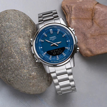 Silver Casio watch with blue face on a gray surface with rocks