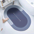 Gray oval bath mat with 'Bathroom' text, placed on the floor beside a bathtub with a foot stepping on it.